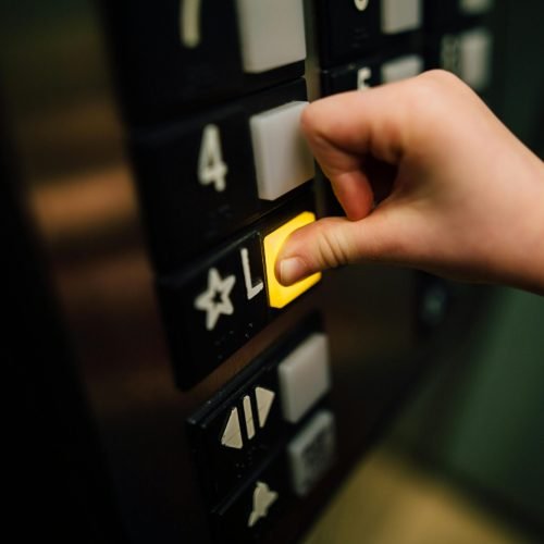 A close-up shot of a hand pushing the 'L' button in an elevator, indoors.