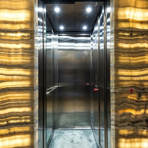 Brightly lit stainless steel elevator with marble walls and modern lighting design.